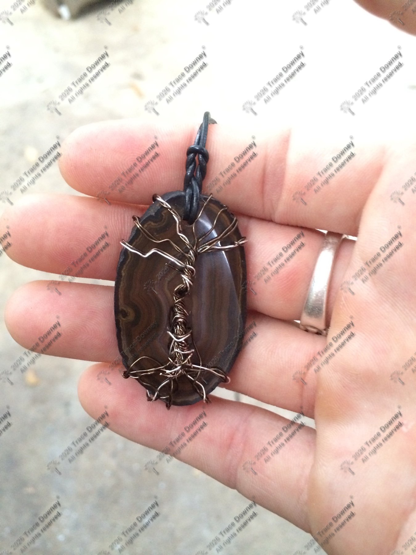 Alternate hand-held view of a dark agate pendant with decorative wire wrapping.