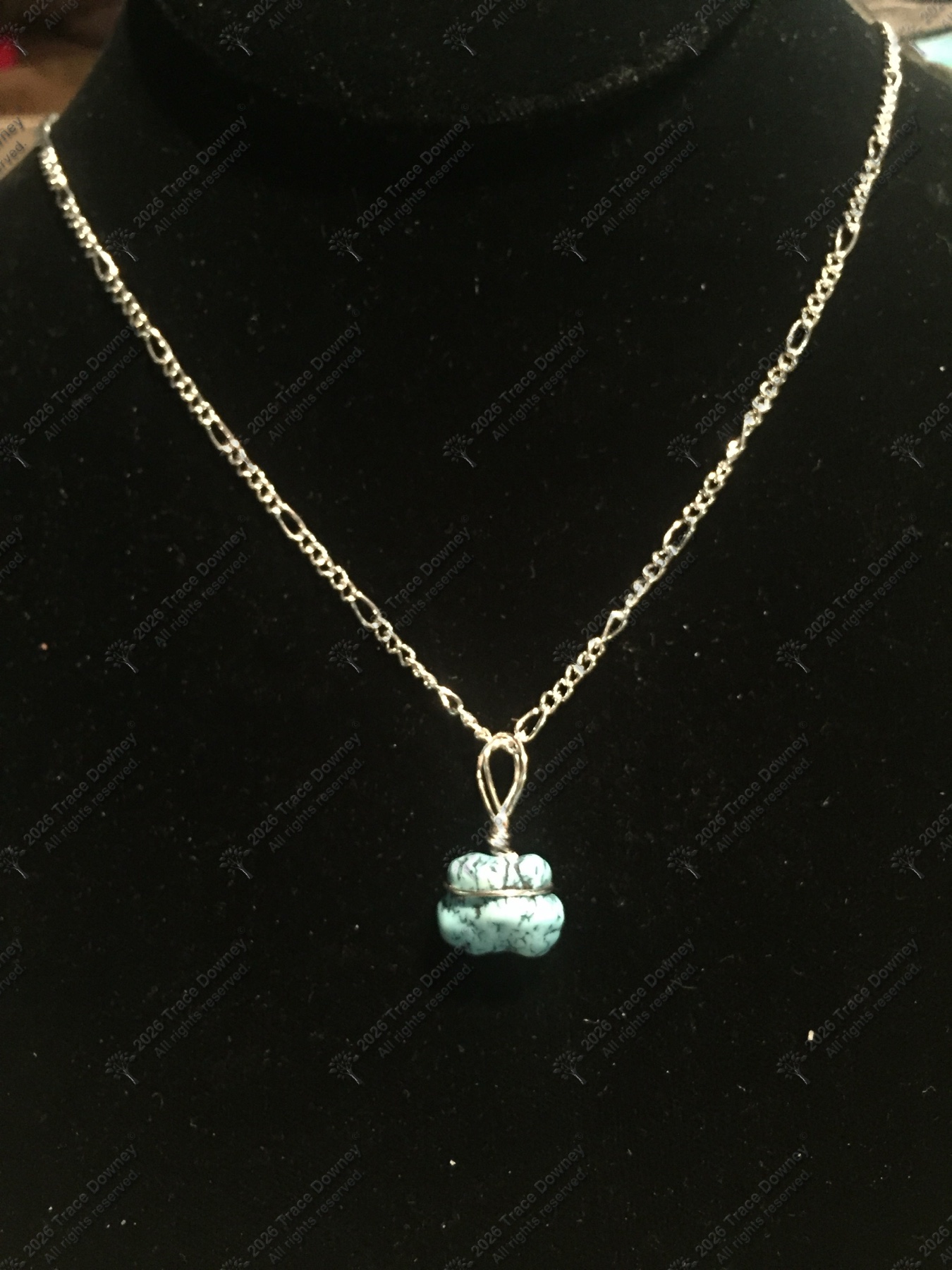 Small blue stone pendant hanging from a delicate silver necklace on a dark display.
