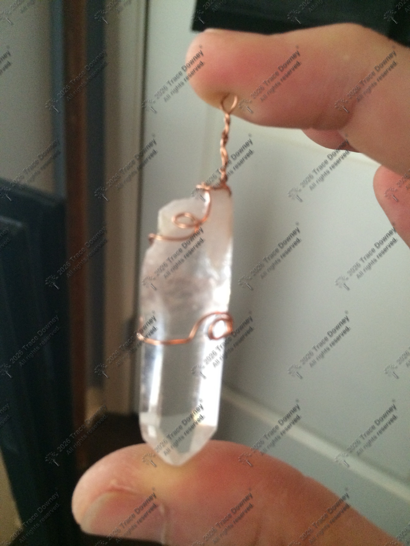 Clear crystal pendant wrapped in copper wire and held between fingers.