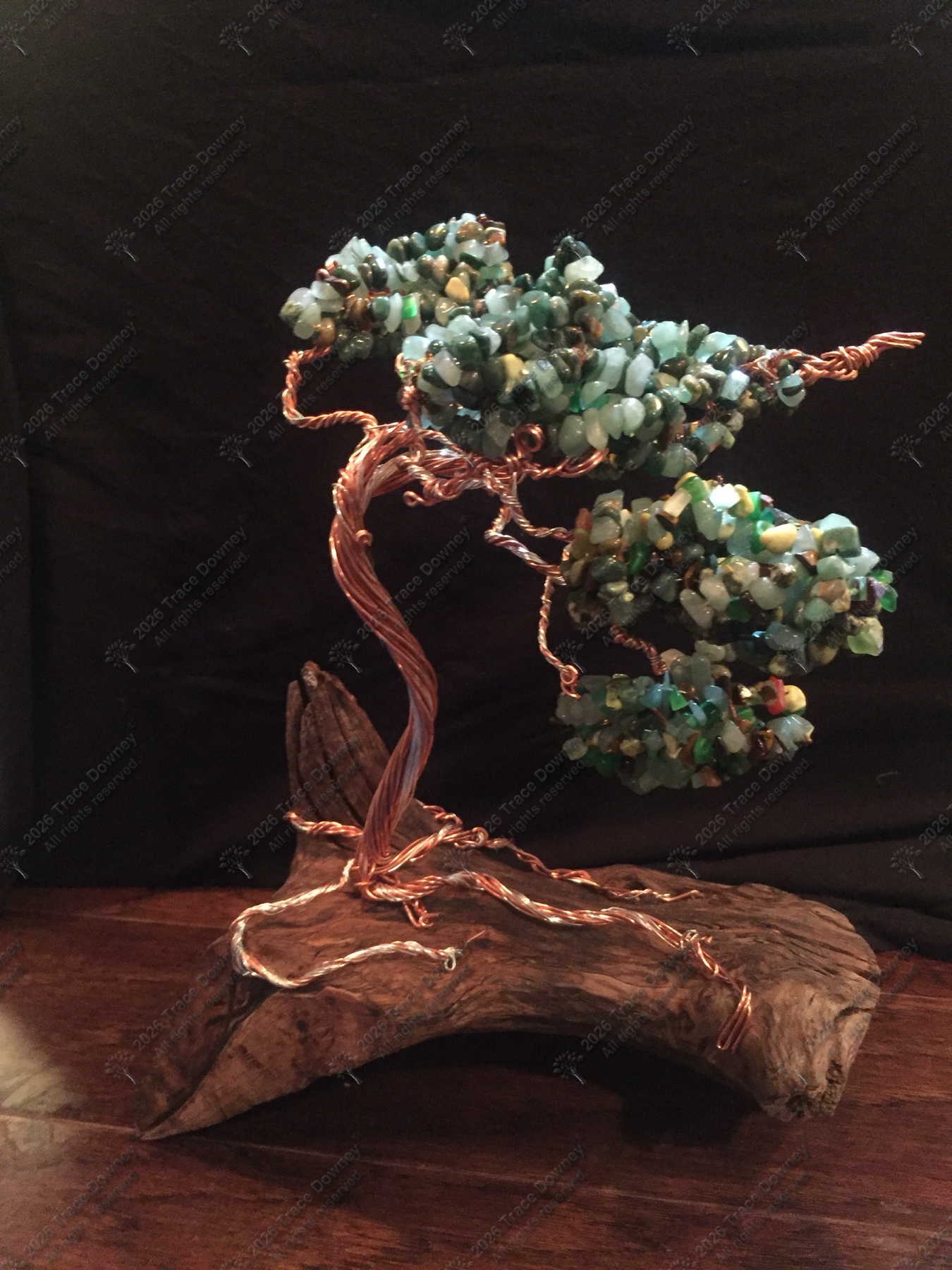 Green stone wire tree sculpture mounted on a natural wood base against a dark backdrop.