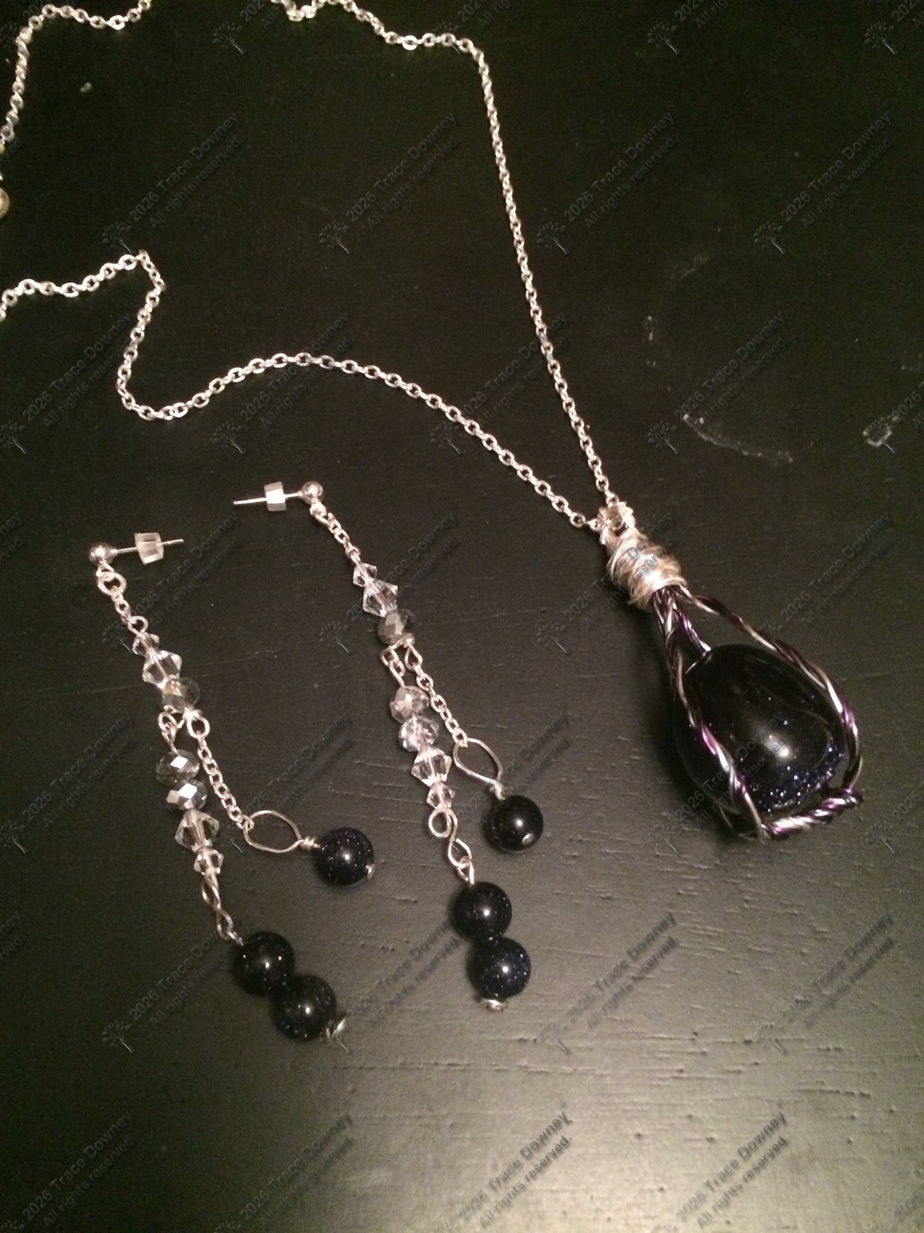 Coordinated dark stone pendant necklace and earrings displayed on a dark surface.