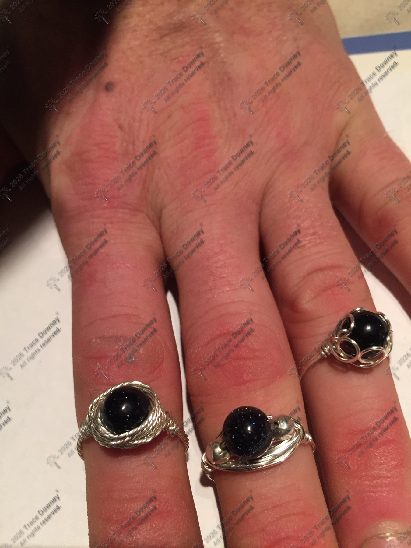 Three dark stone rings worn on a hand.