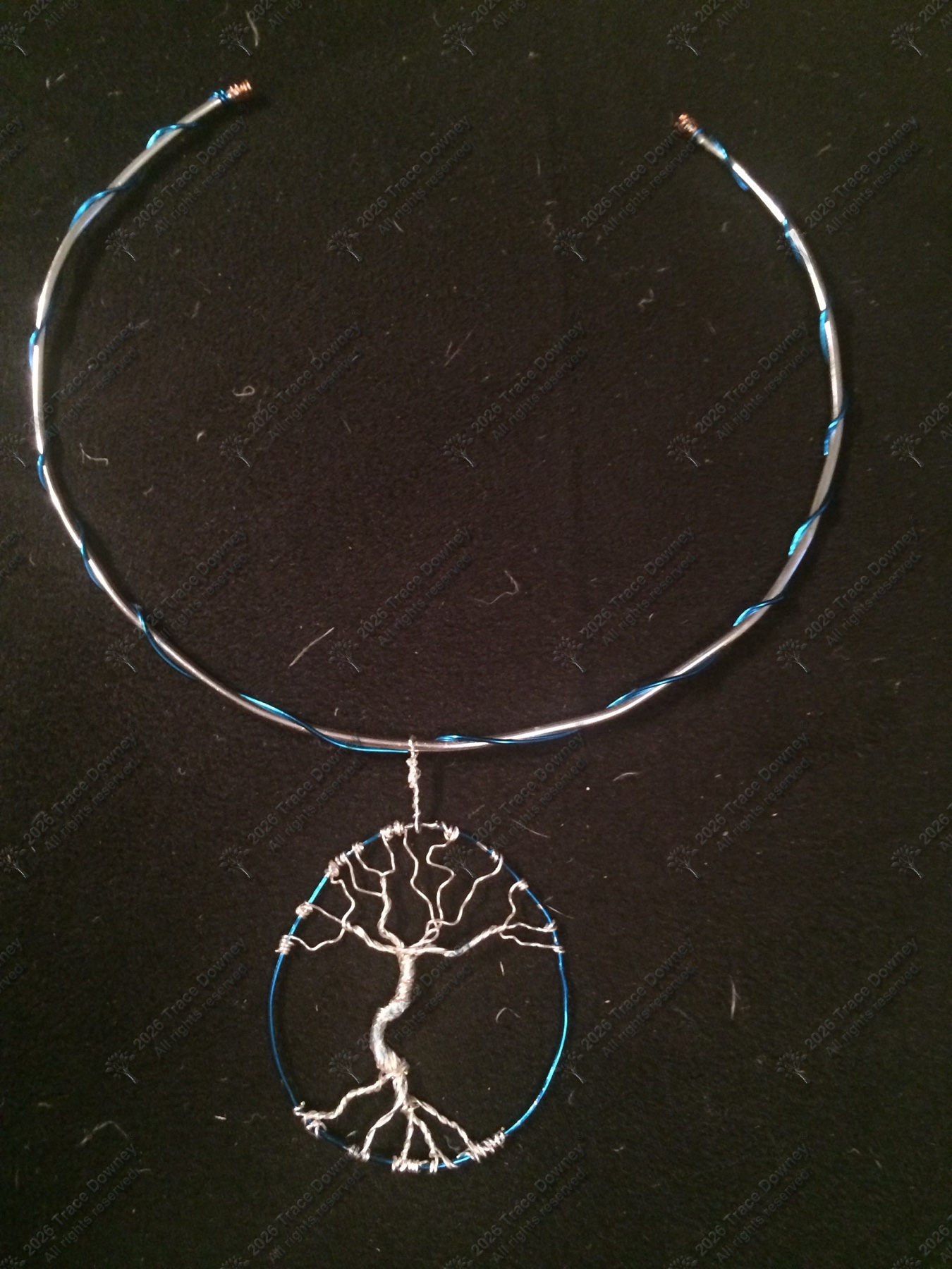 Wire tree of life pendant inside a blue circular frame against a dark background.