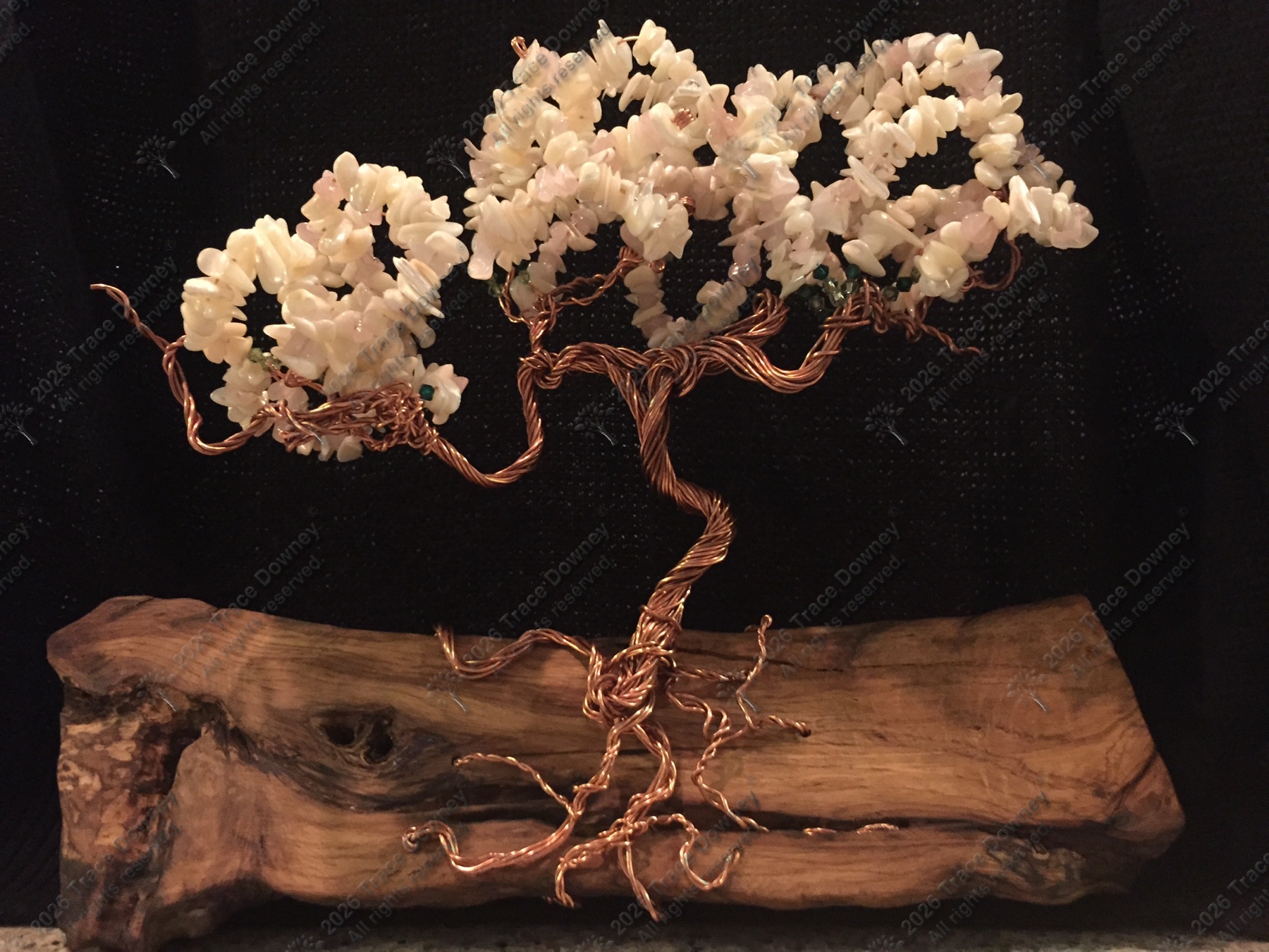 White blossom wire tree against a dark backdrop on a wood base.