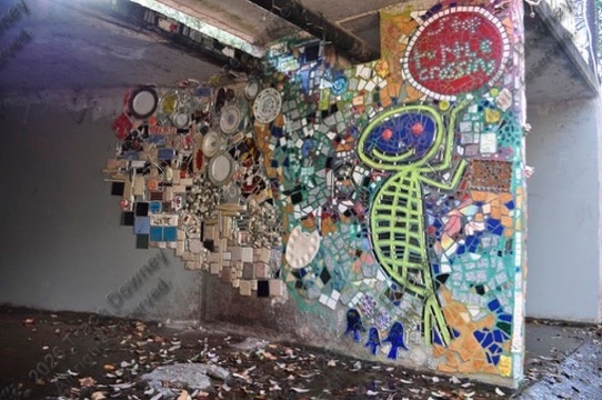 A colorful mosaic wall photographed at an angle inside an industrial space.