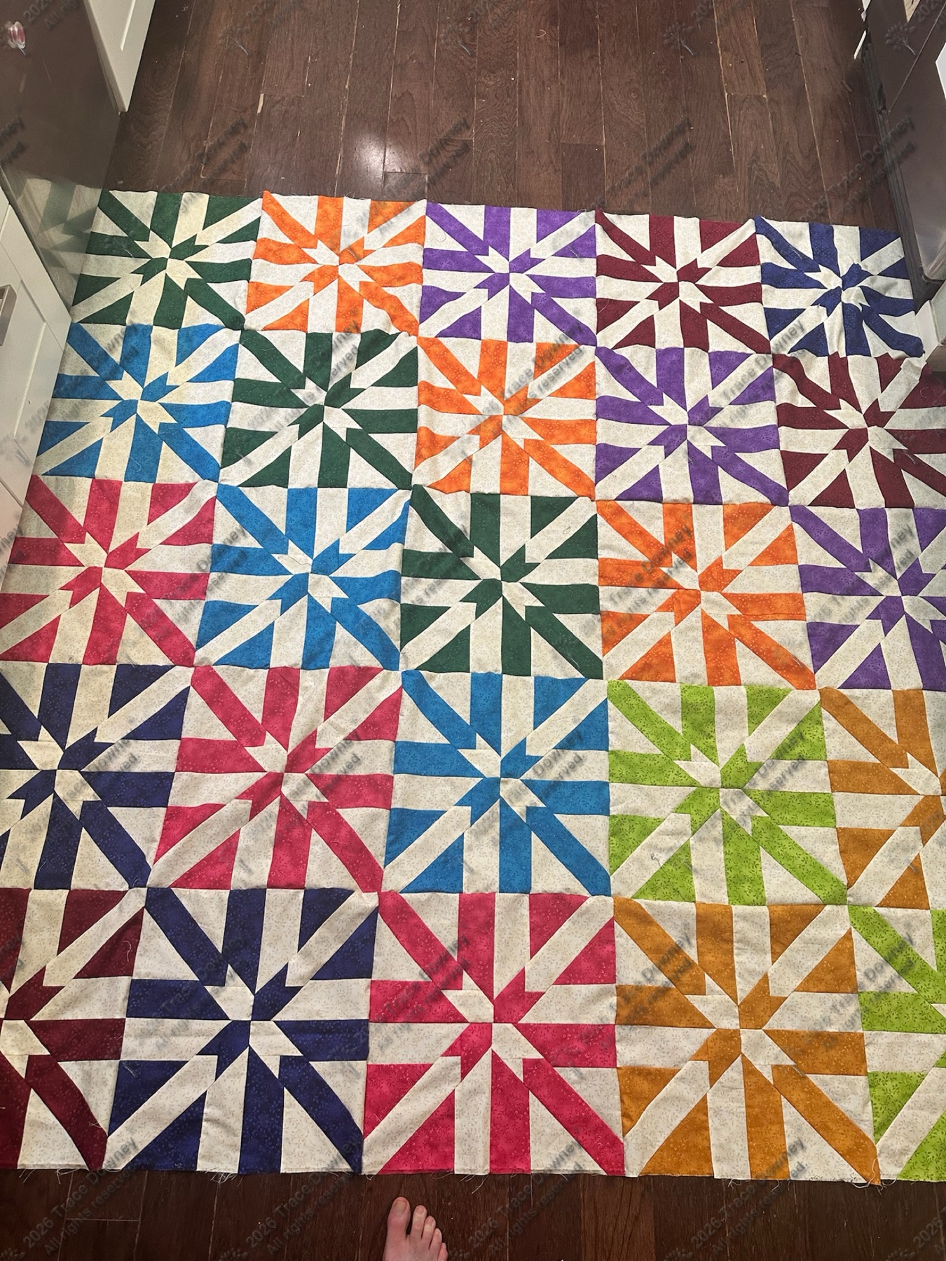 Vertical quilt with rainbow pinwheel blocks arranged in a repeating grid.