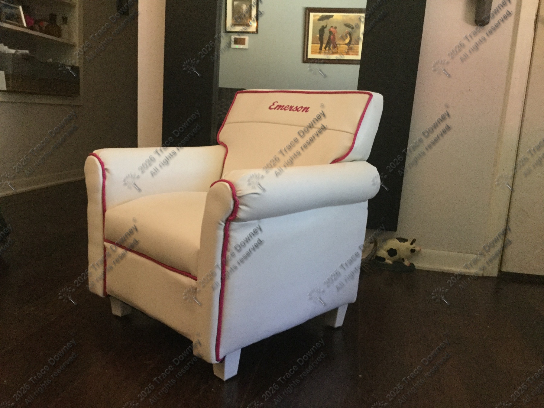 Finished white upholstered chair with red piping and Emerson embroidery on the headrest.